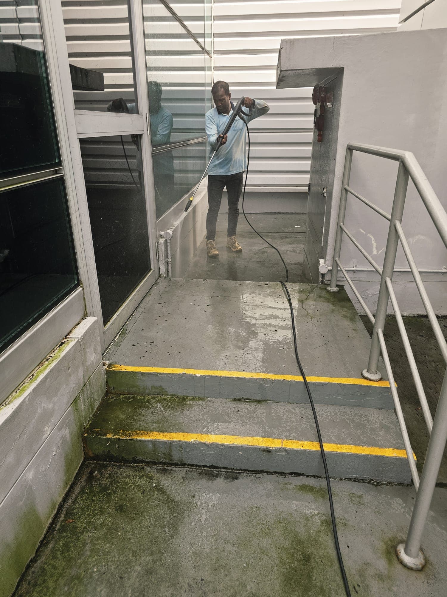 Hydroseal rope-access technician pressure washing a high-rise glass and cladding façade in Singapore