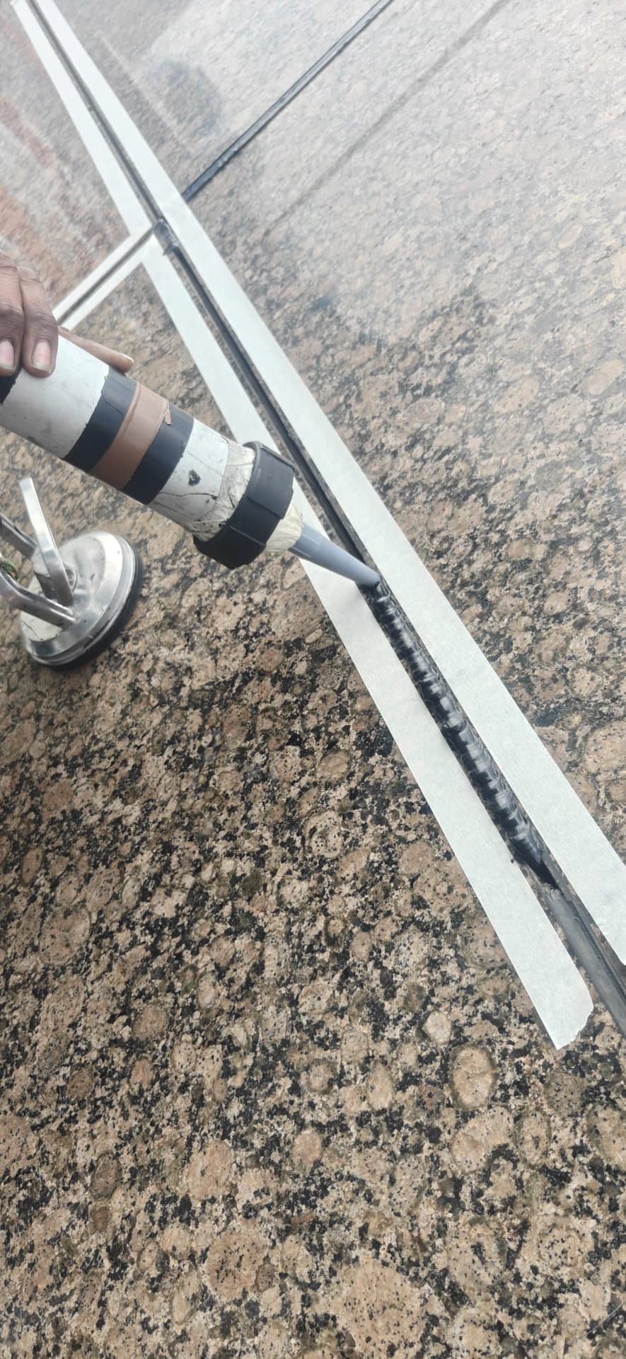 Close-up of a Hydroseal technician gunning fresh grey polyurethane sealant into a façade joint over granite cladding during rope-access recurrence works in Singapore