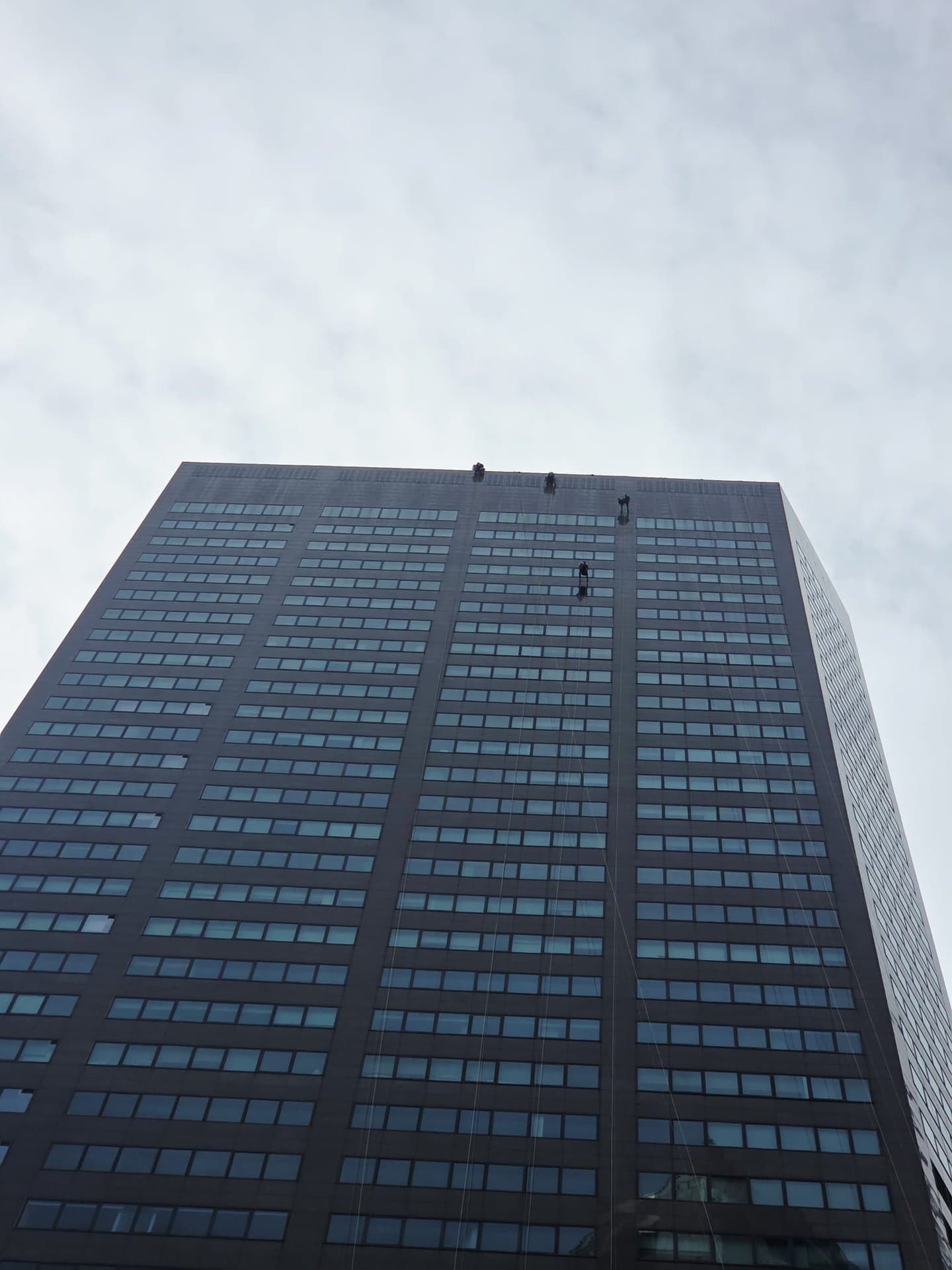 Upward view of a tall residential tower in Singapore with Hydroseal IRATA rope-access technicians abseiling the façade during sealant works