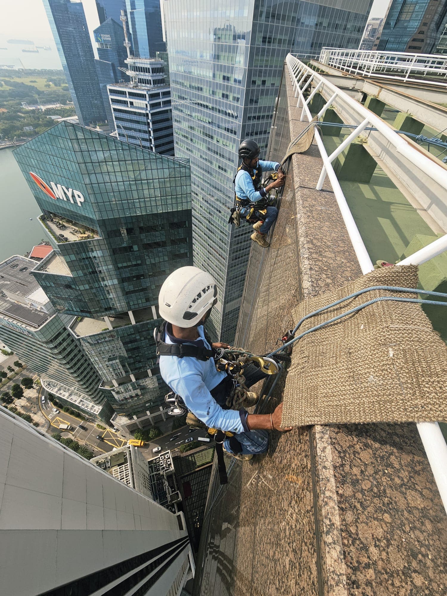 Rope-access technician descending a tower façade with the Marina Bay skyline behind