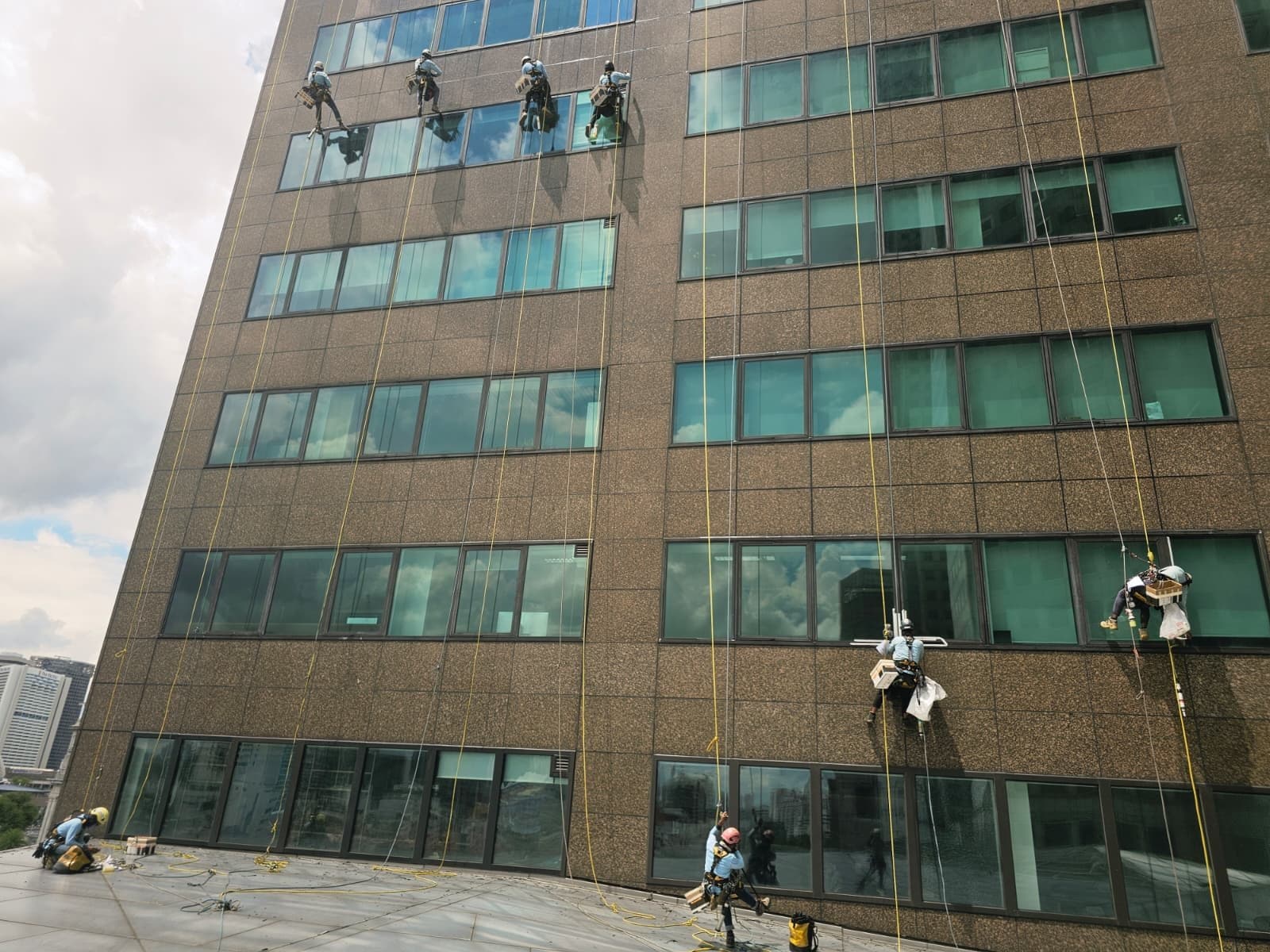 Multiple Hydroseal IRATA rope-access technicians abseiling across several floors of a granite-and-glass office building façade in Singapore
