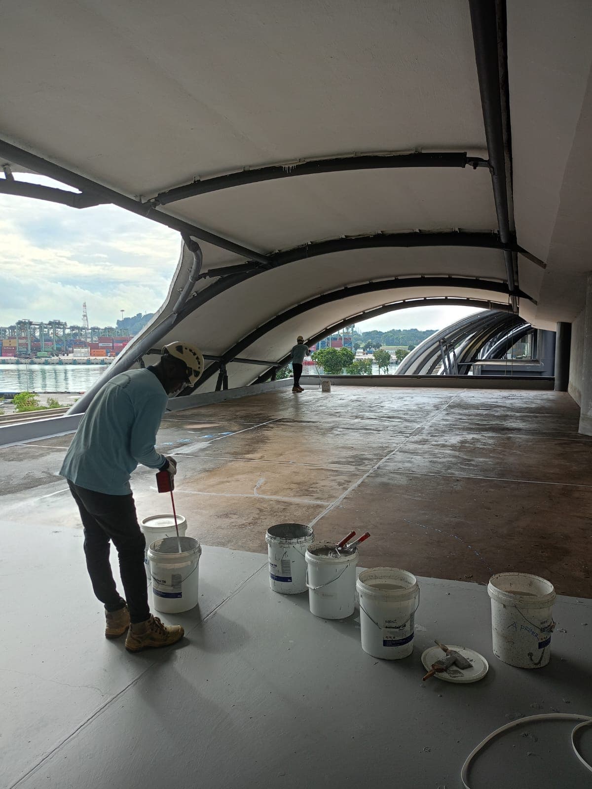 Hydroseal technician preparing waterproofing materials on a concrete deck at a Singapore waterfront pavilion