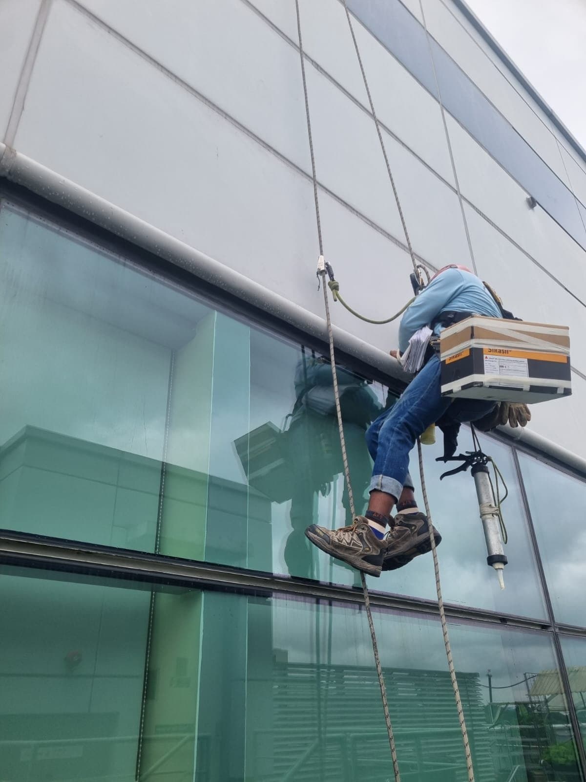 Hydroseal IRATA rope-access technician abseiling a glass curtain-wall façade and applying sealant during waterproofing works on a seafront condominium in the East Coast area of Singapore